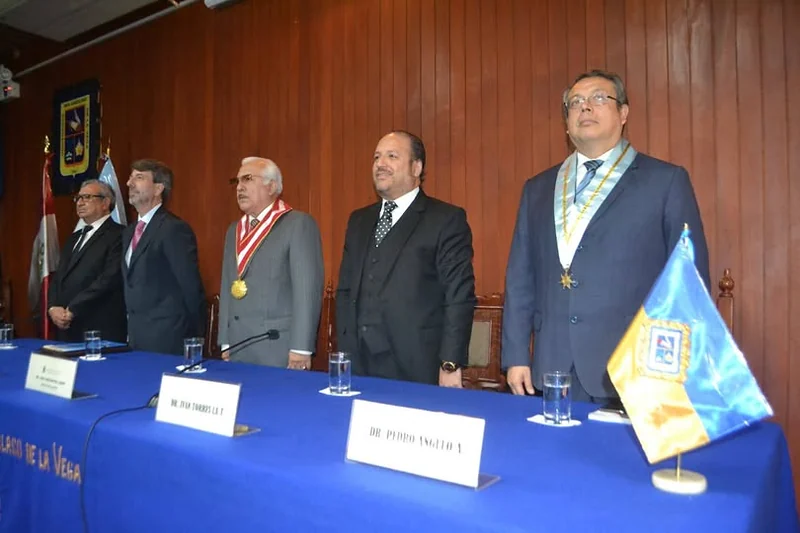 Autoridades de pie ante la mesa de honor durante la ceremonia de distinción de la UIGV.