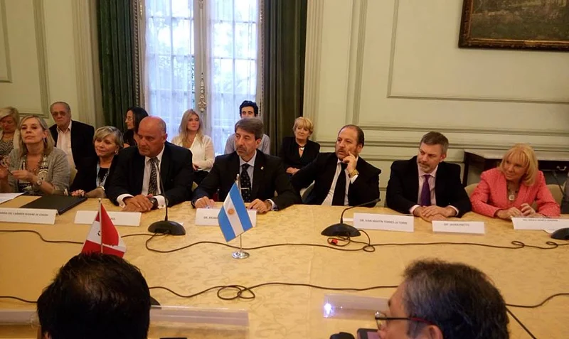 Mesa de reunión en un salón, con las banderas del Perú y de la Argentina, placas con nombres y micrófonos